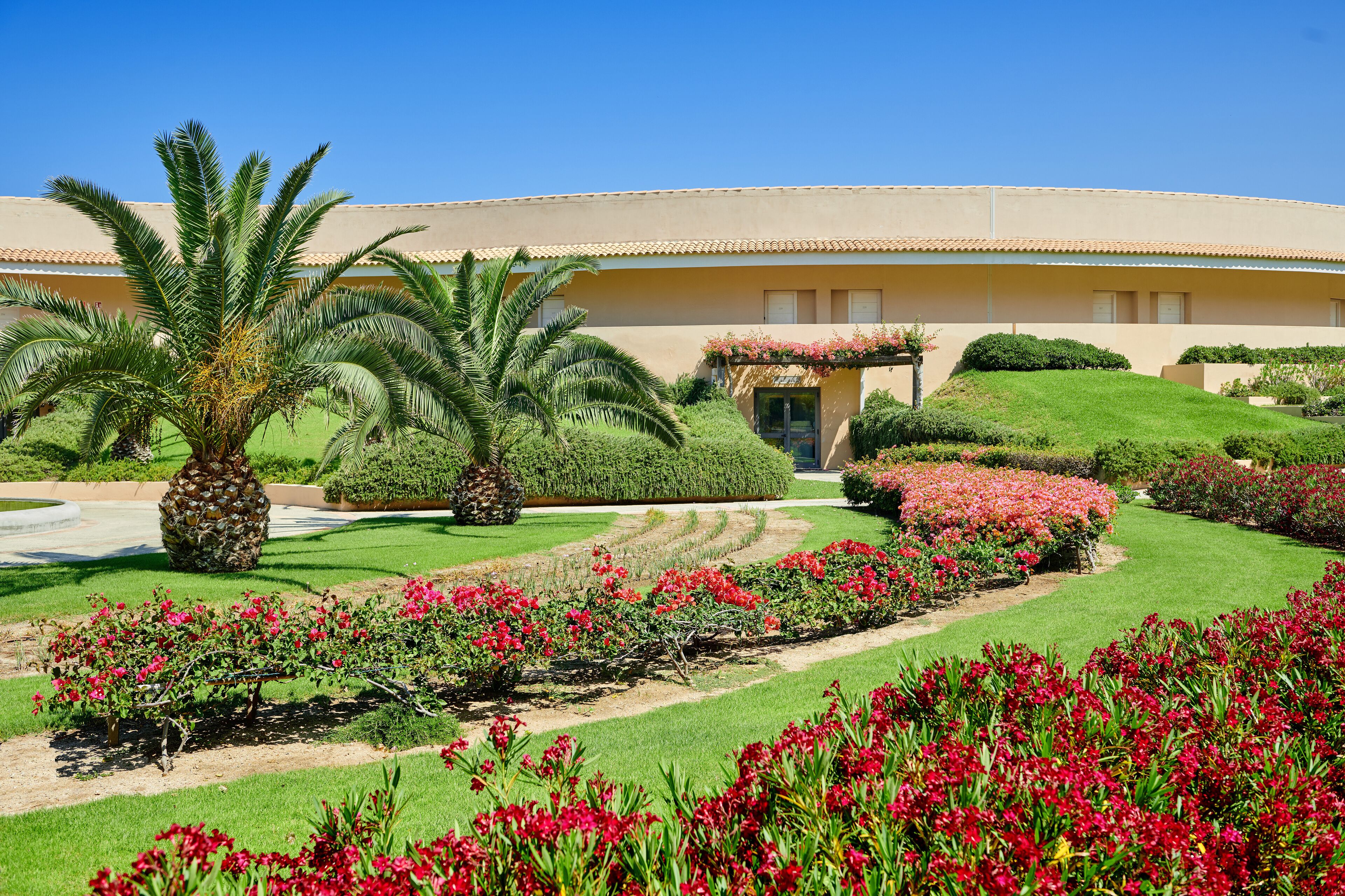 A hotel with a well-maintained garden, palm trees, and a variety of flowering plants.