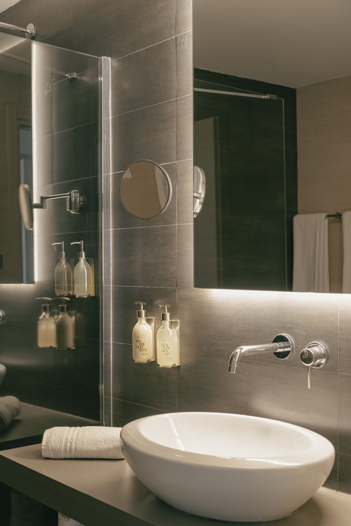A modern bathroom with a large mirror, a white sink, and toiletries on the wall.