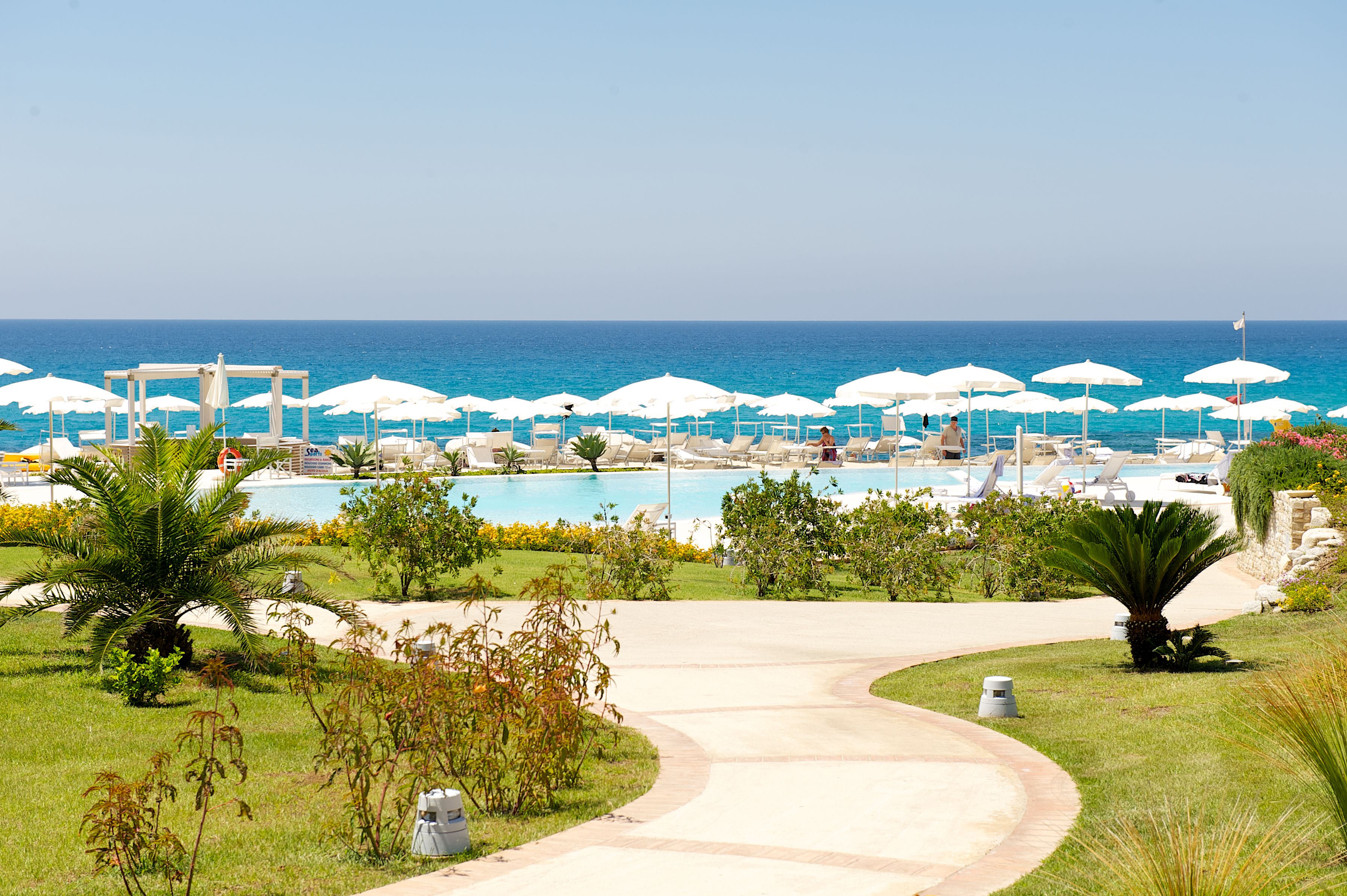 A resort with a pool area, white umbrellas, and a view of the ocean.