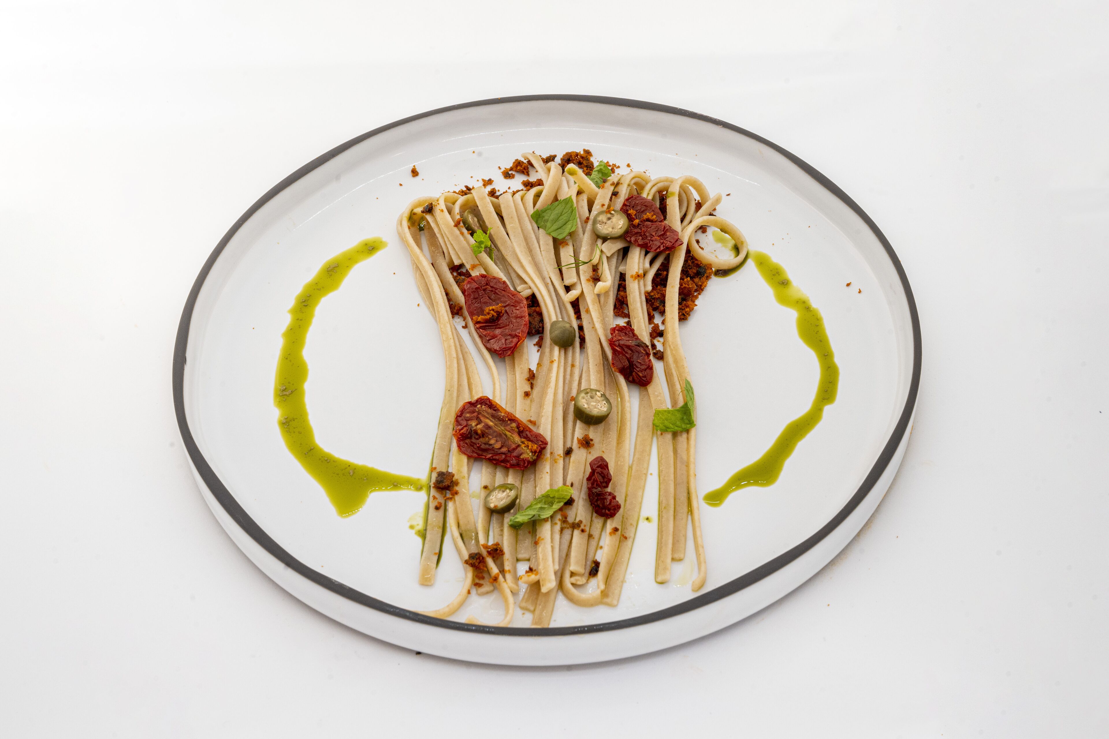 A plate of pasta with green olives, sun-dried tomatoes, and basil leaves.