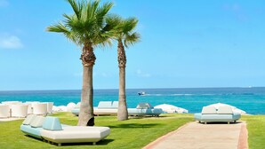 A beachside lounge area with white lounge chairs and a palm tree. - Capovaticano Resort Thalasso Spa (Ricadi)