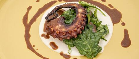 A plate with octopus, greens, and sauce.