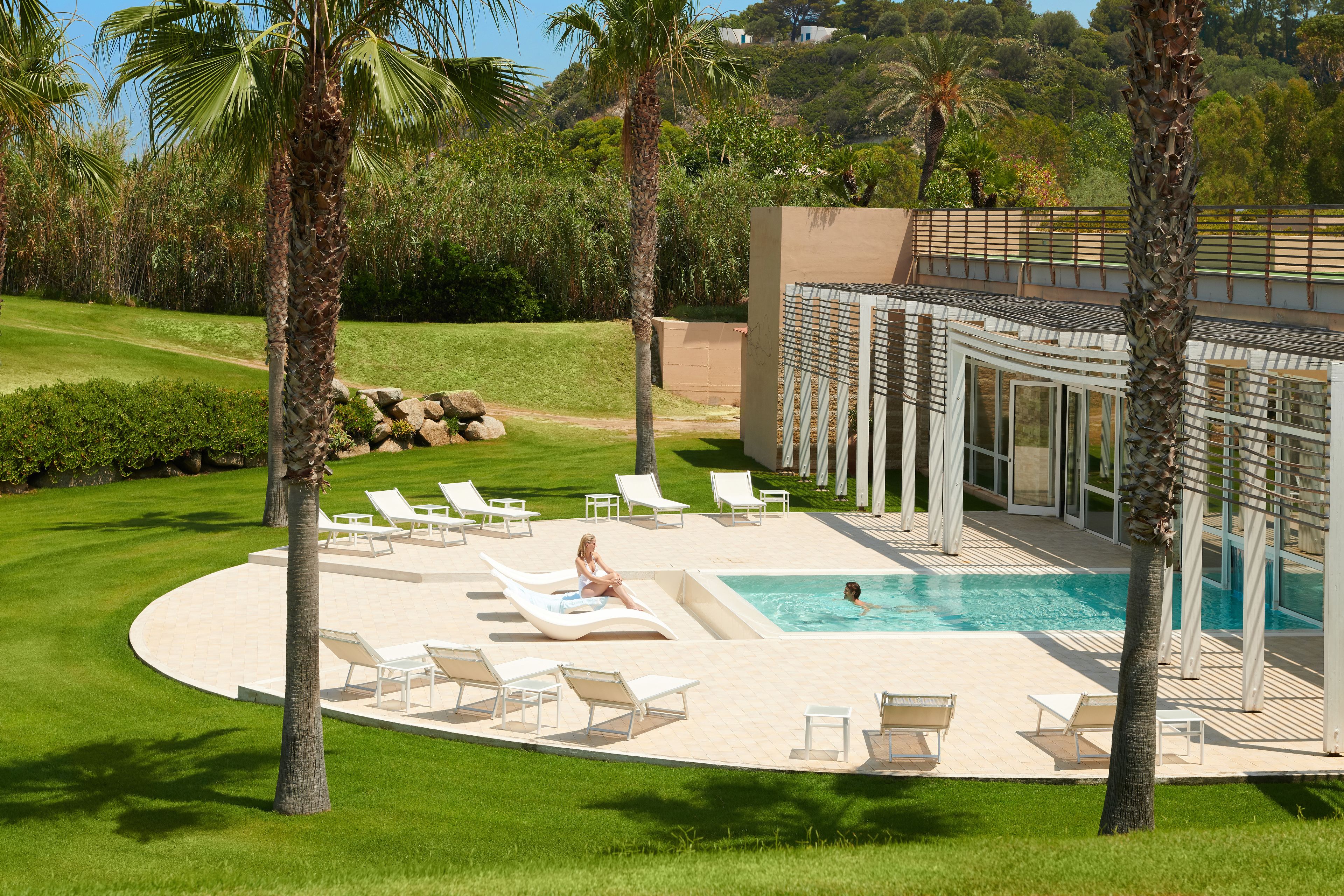 A pool area with lounge chairs, a swimming pool, and a building with large windows.