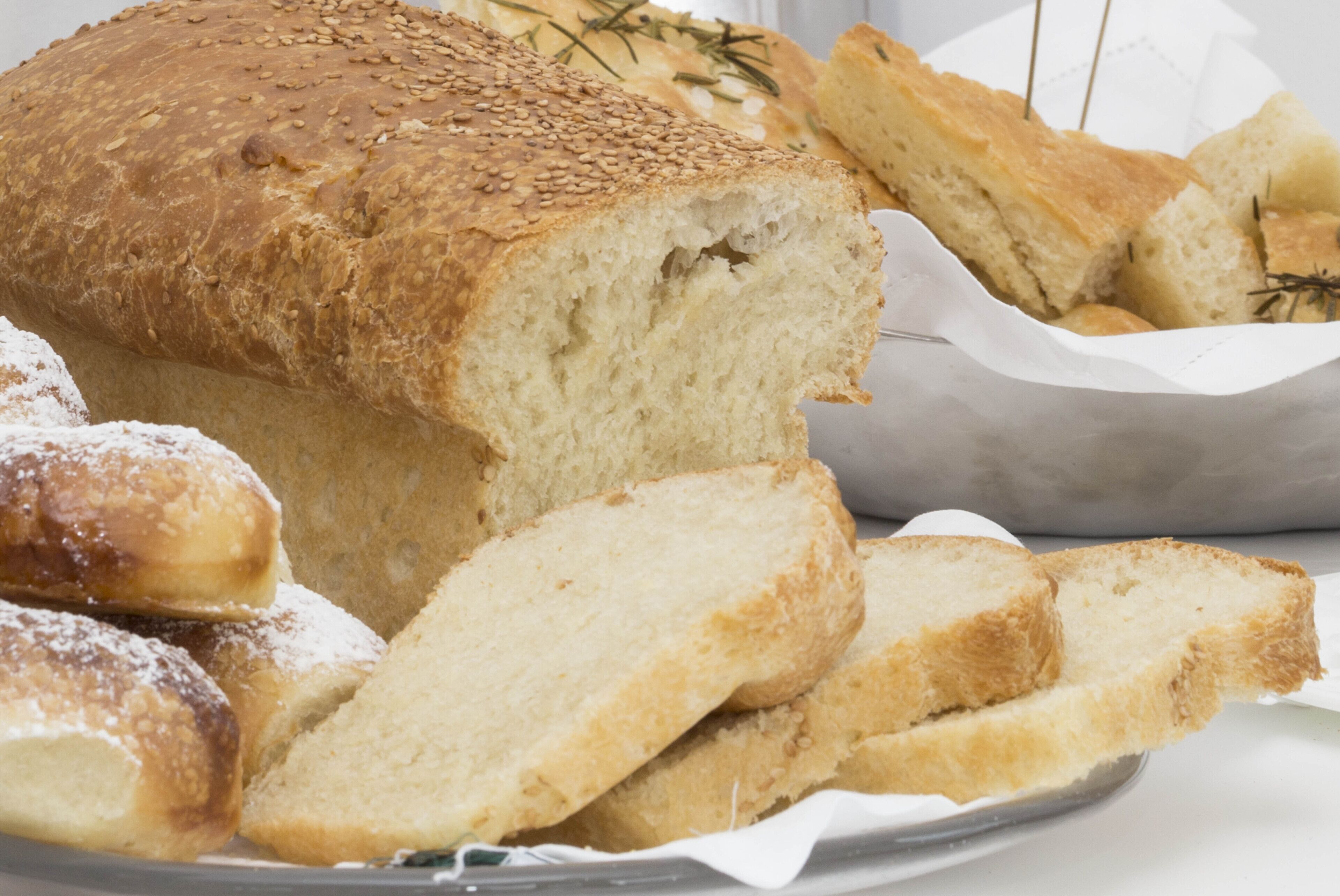A loaf of bread with sliced pieces and a basket of bread rolls.
