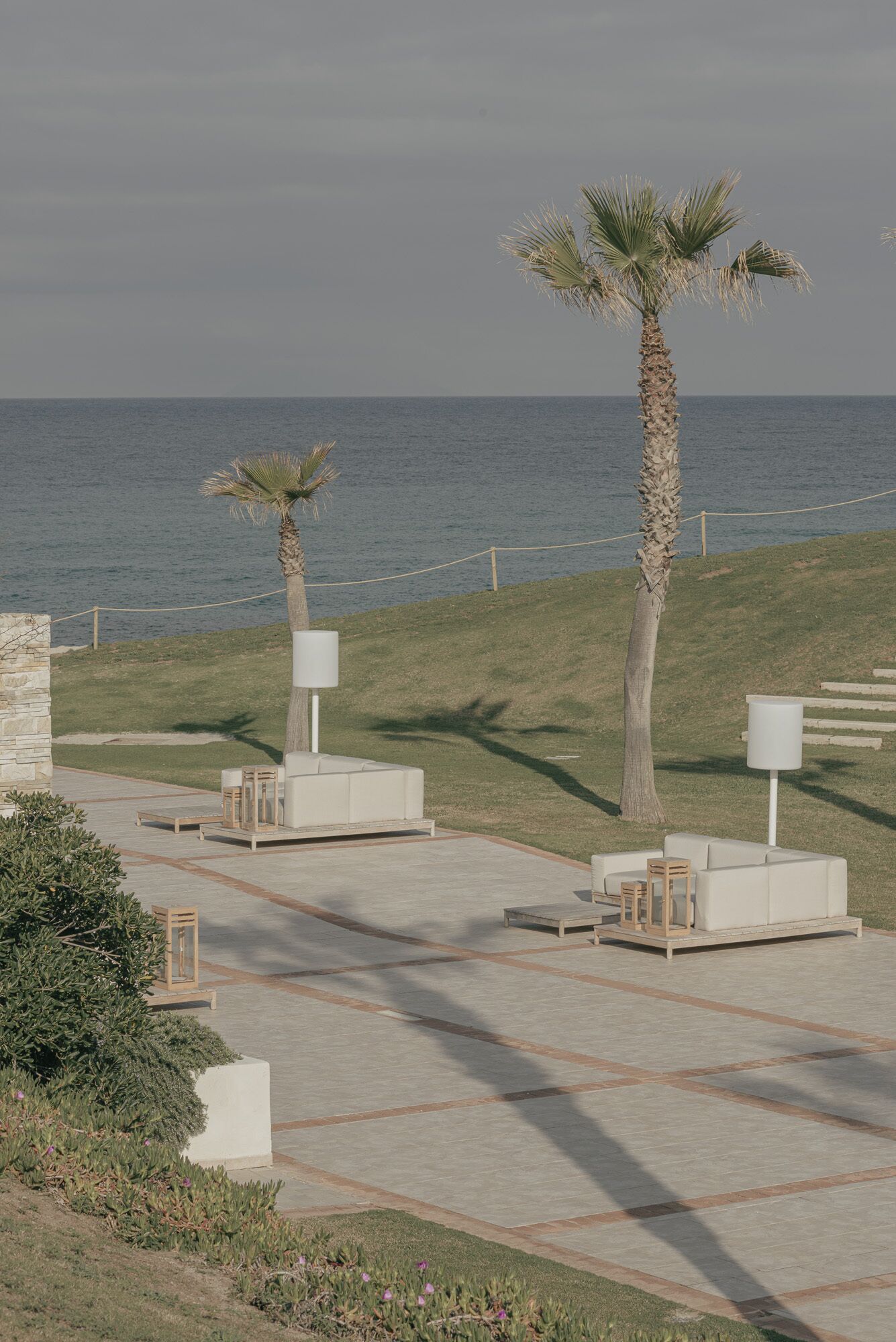 A coastal walkway with palm trees, outdoor seating, and a view of the sea.