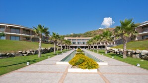 A hotel with a central courtyard, palm trees, and a mountain backdrop. - Capovaticano Resort Thalasso Spa (Ricadi)
