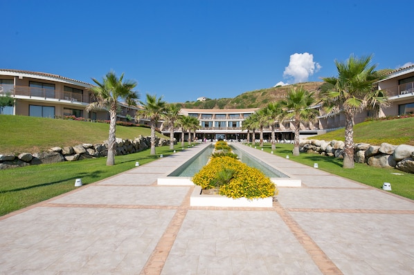 A hotel with a central courtyard, palm trees, and a mountain backdrop. - Capovaticano Resort Thalasso Spa (Ricadi)