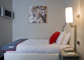 Camera d'albergo con un letto, un comodino, un telefono, una lampada e un quadro di un cavallo.