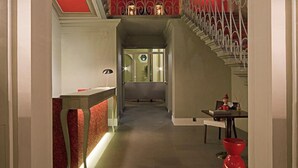 A hallway with a staircase, a reception desk, and a red accent wall. - Hotel Rosso 23 (Florence)