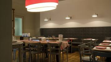 Um restaurante com soalho de madeira, mesas com jogos americanos vermelhos e uma luminária pendente vermelha.