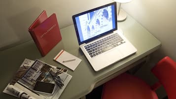 Una computadora portátil sobre un escritorio con una lámpara, una carpeta roja, un cuaderno y un teléfono inteligente.