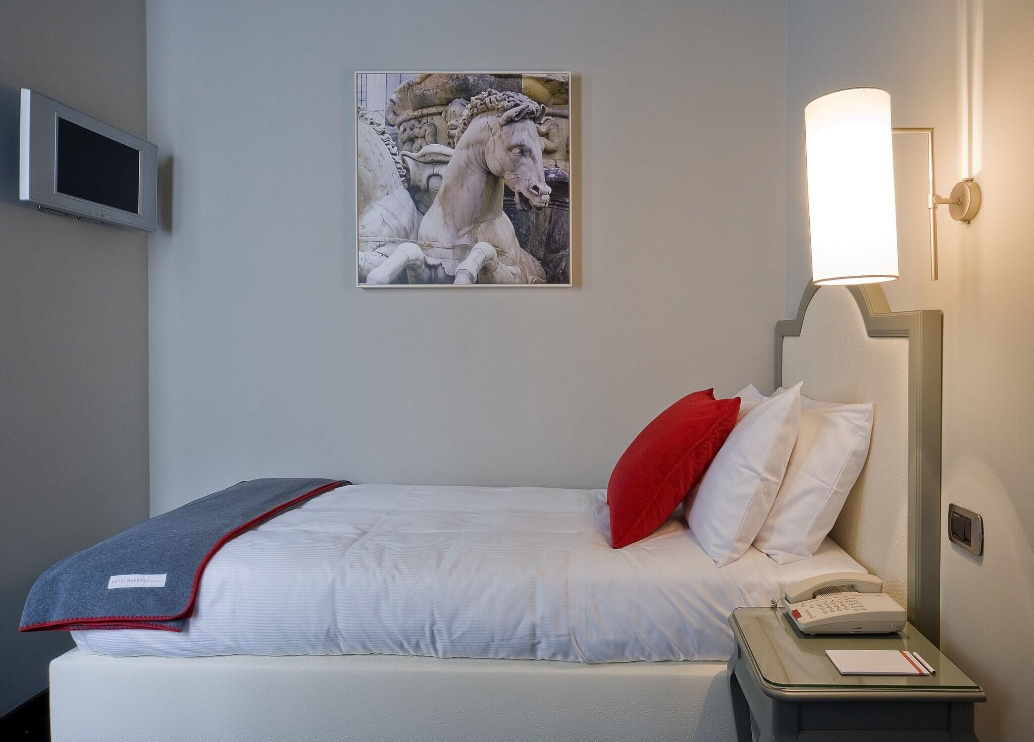 A hotel room with a bed, a bedside table with a lamp, a telephone, and a picture on the wall.