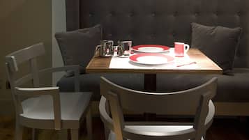 Een eethoek met een tafel gedekt voor twee personen, een comfortabele bank en een wandlamp.