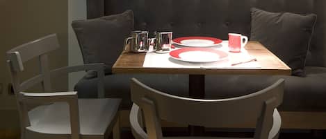 Un comedor con una mesa preparada para dos personas, un banco acolchado y una lámpara fijada a la pared.