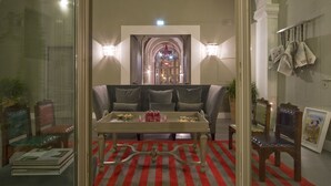 A room with a dining table, sofa, and chairs, a red and gray striped carpet, and a view of a grand staircase. - Hotel Rosso 23 (Florence)