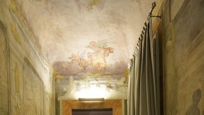 A corridor with wooden flooring, a bench, and a wall with a mural. - Hotel Rosso 23 (Florence)