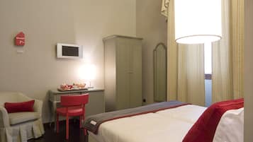 Quarto de hotel com uma cama, uma escrivaninha com cadeira, televisão e guarda-roupa.
