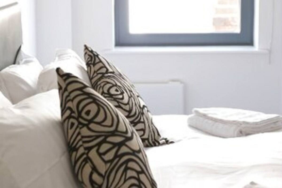 Een slaapkamer met een bed, witte beddengoed en een raam met uitzicht.