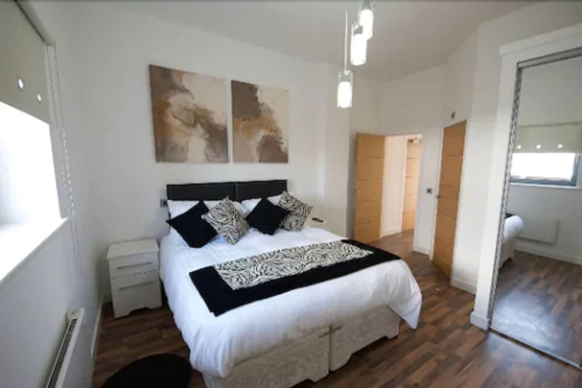 Een slaapkamer met een bed, nachtkastjes, kunst aan de muur en een deur die naar een andere kamer leidt.