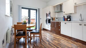 A modern kitchen with white cabinets, a built-in oven, and a dining area with wooden chairs and a table.