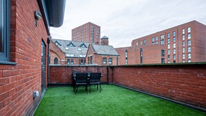 A rooftop terrace with artificial grass, brick walls, and a table with chairs.