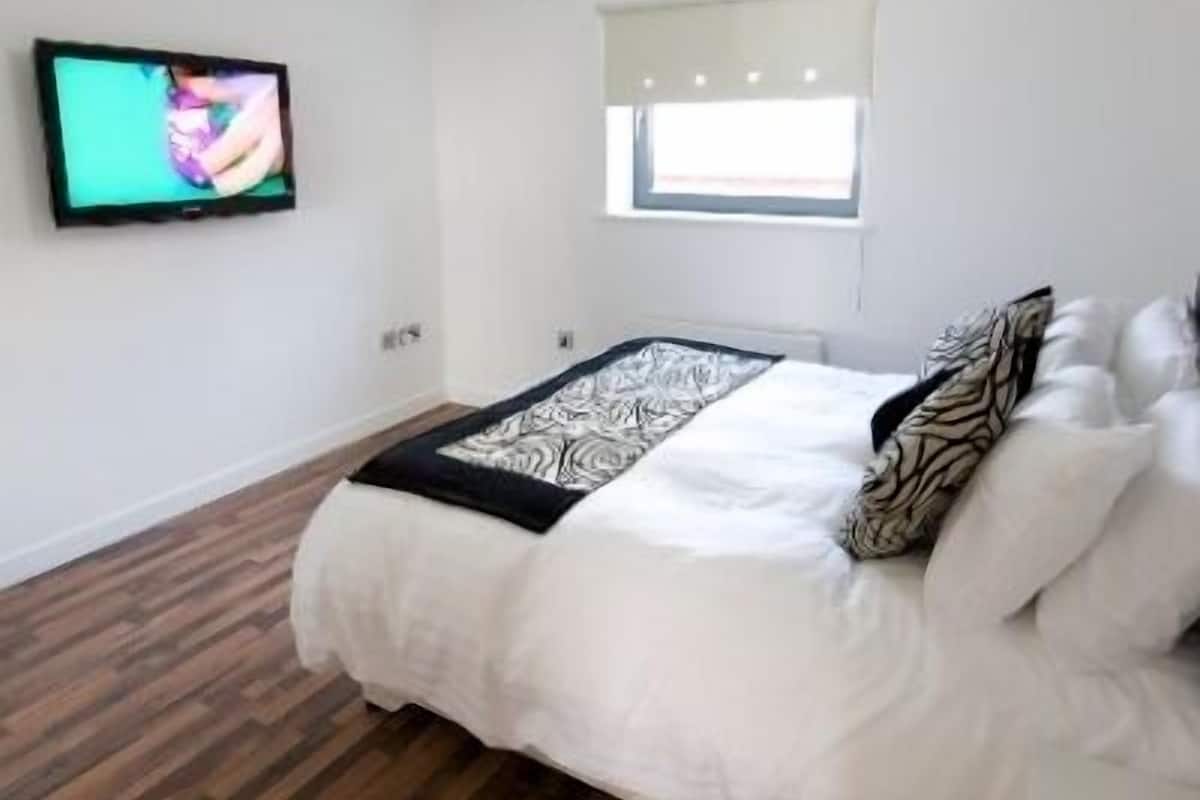 Een slaapkamer met een bed, een televisie aan de muur, een raam en een plafondlamp.