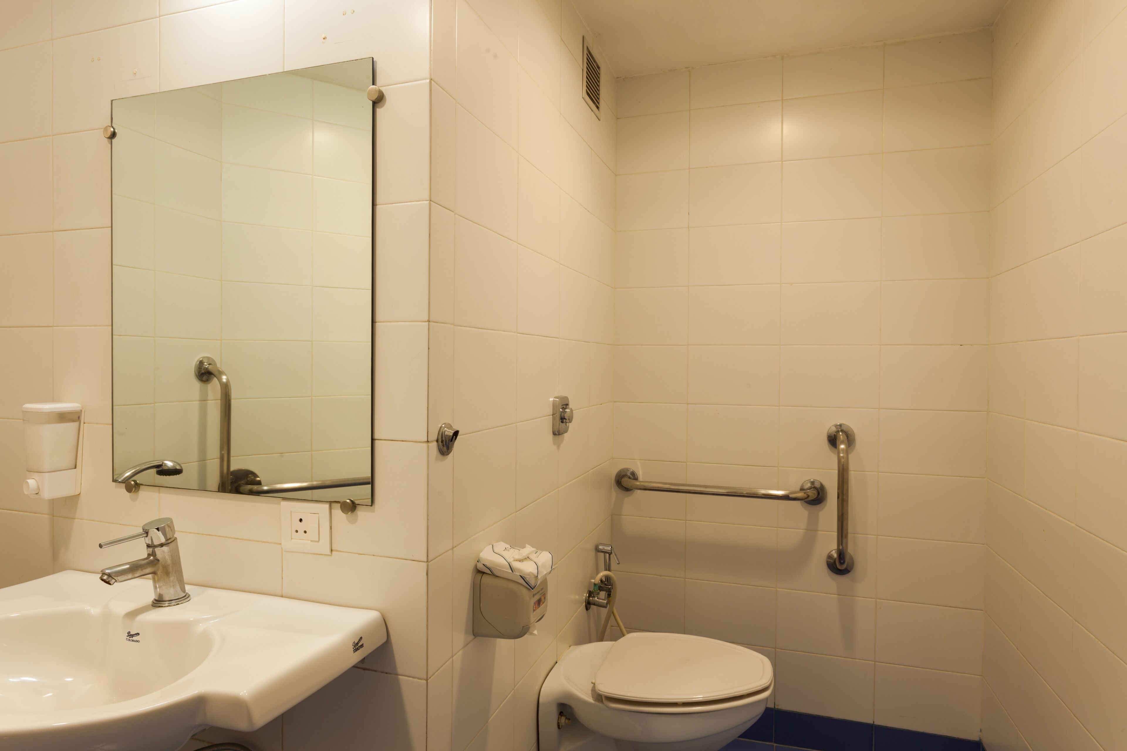 A bathroom with a sink, mirror, toilet, and grab bars.