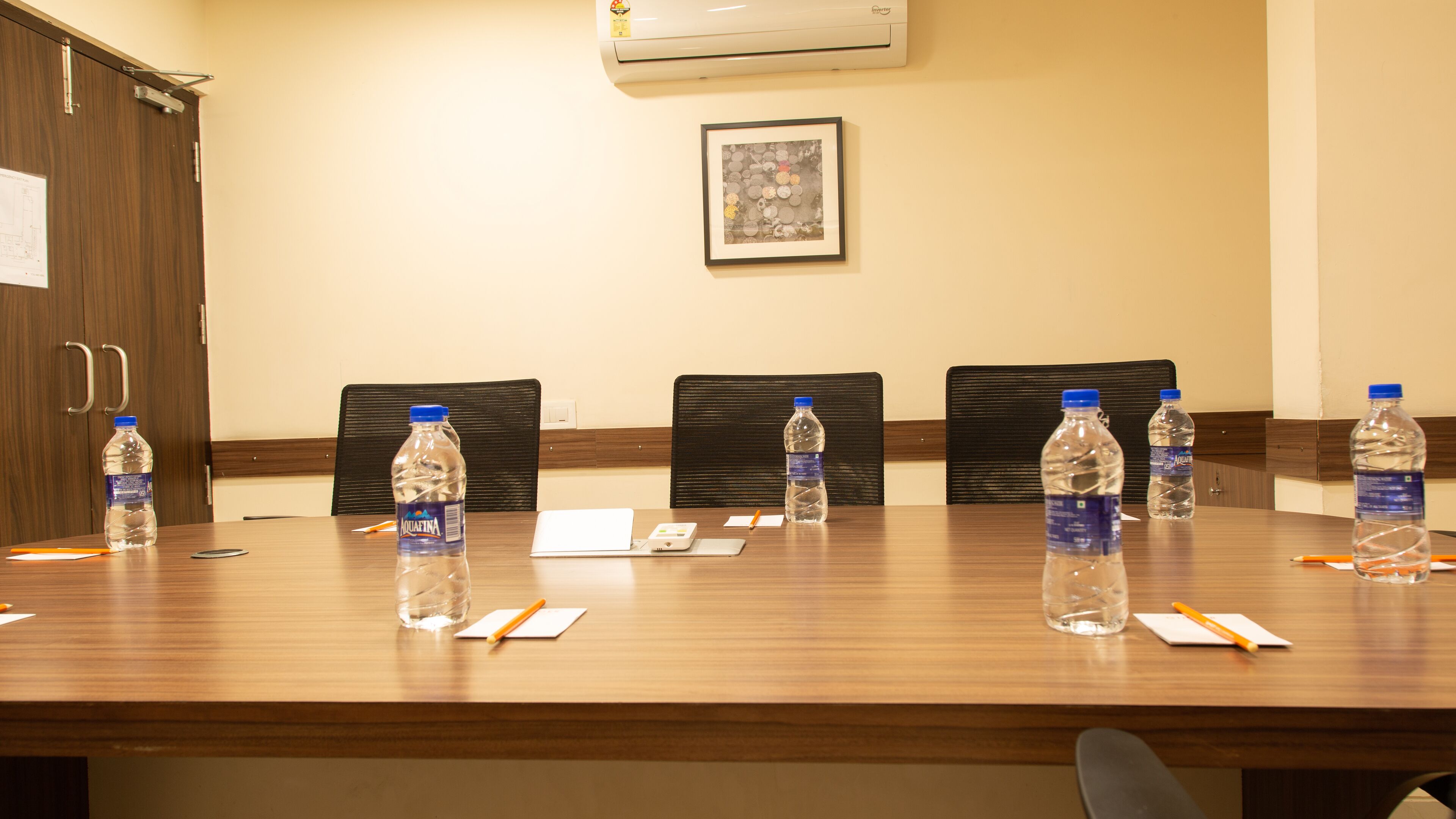 A conference room with a wooden table, chairs, water bottles, a laptop, and a framed picture on the wall.