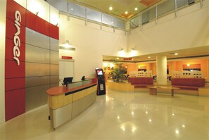 Un moderno vestíbulo de hotel con una recepción, una zona de estar y una planta grande.