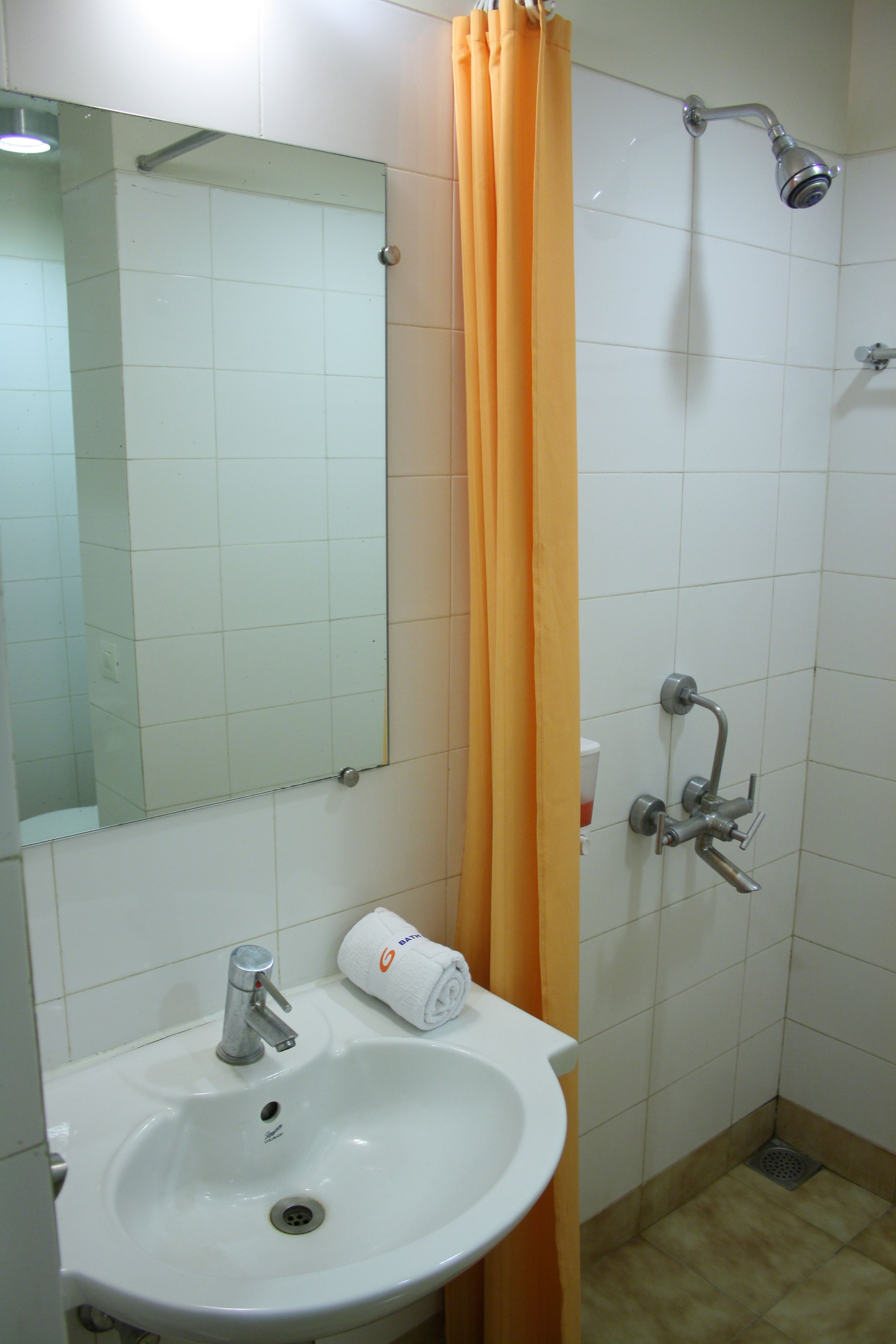 Baño con lavamanos, espejo, ducha y cortina de ducha naranja.
