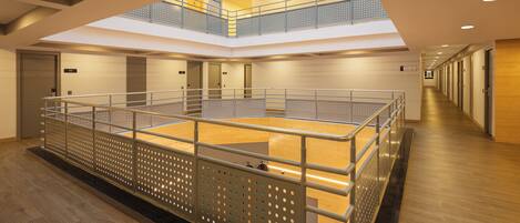 A spacious indoor area with a mezzanine level, wooden flooring, and metal railings.