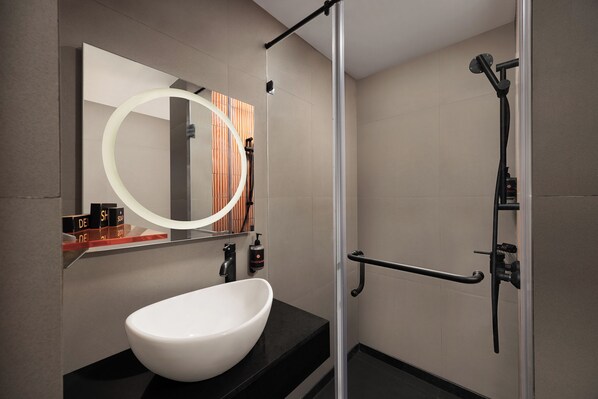 A modern bathroom with a large white sink, a mirror with a circular light, and a shower area with a handheld showerhead.