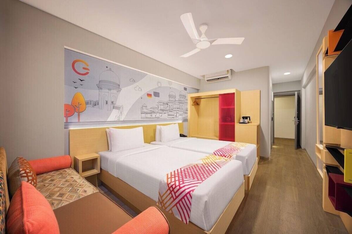 A hotel room with two beds, a ceiling fan, an air conditioning unit, a wardrobe, and a television.