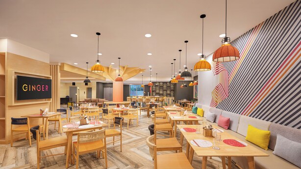 Un restaurante moderno con mesas y sillas de madera, lámparas colgantes y una pared a rayas.
