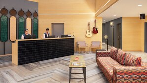 Un área de recepción moderna con un mostrador negro, dos empleados, una guitarra y un sofá estampado.