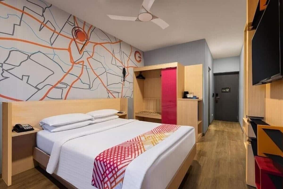 A hotel room with a bed, a desk, a chair, a wardrobe, and a wall with a map design.