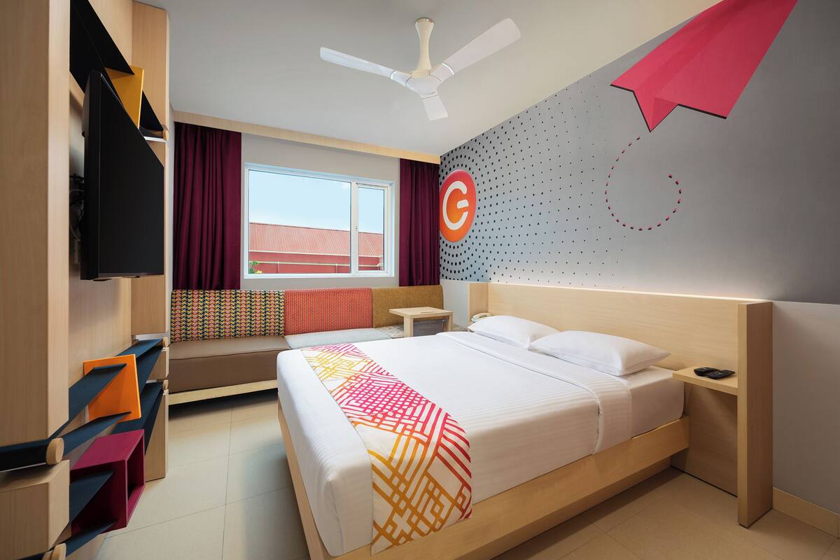 A modern hotel room with a bed, a desk, a TV, and a window with curtains.