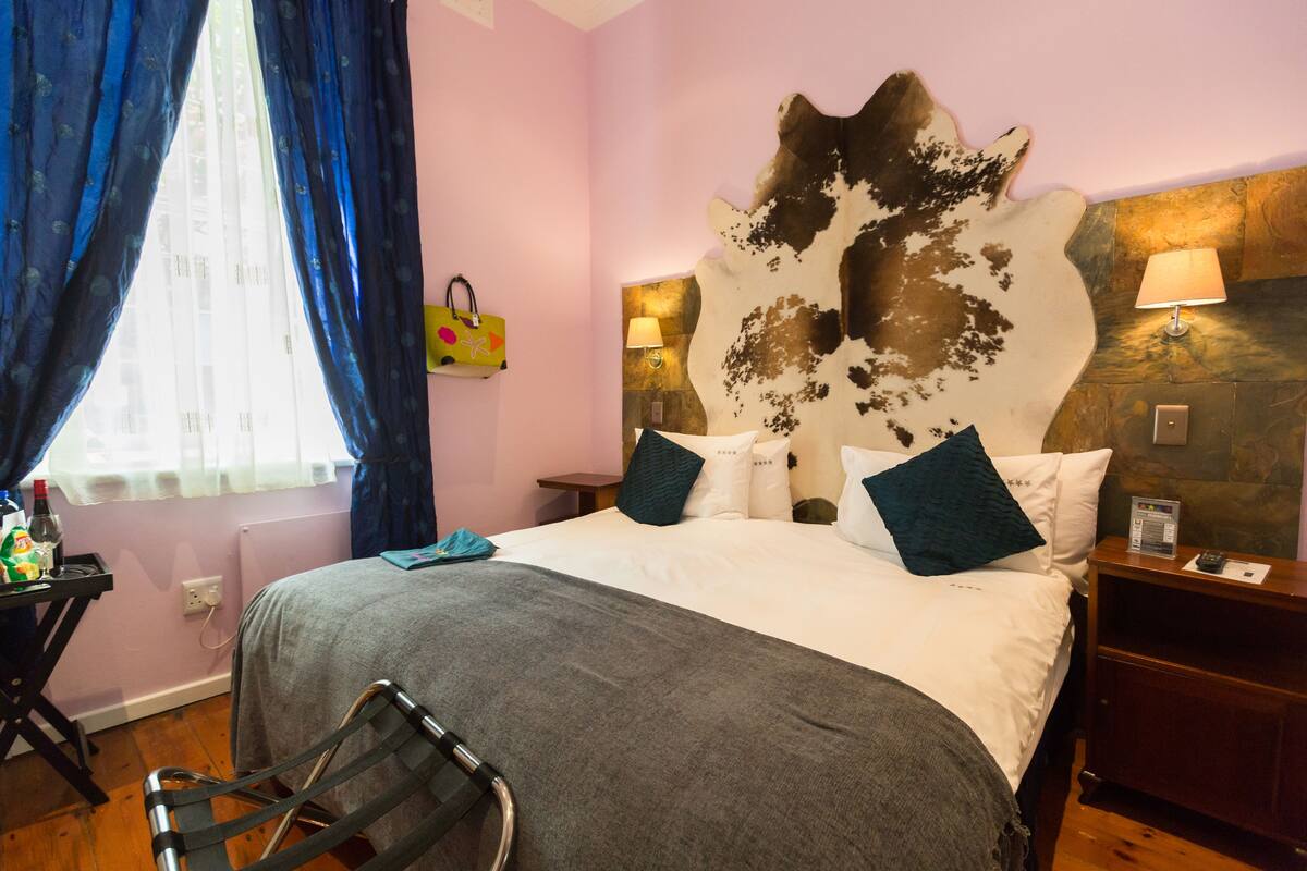Quarto de hotel com uma cama, cabeceira estampada com padrão de animal, mesa de cabeceira com abajur e janela com cortinas.