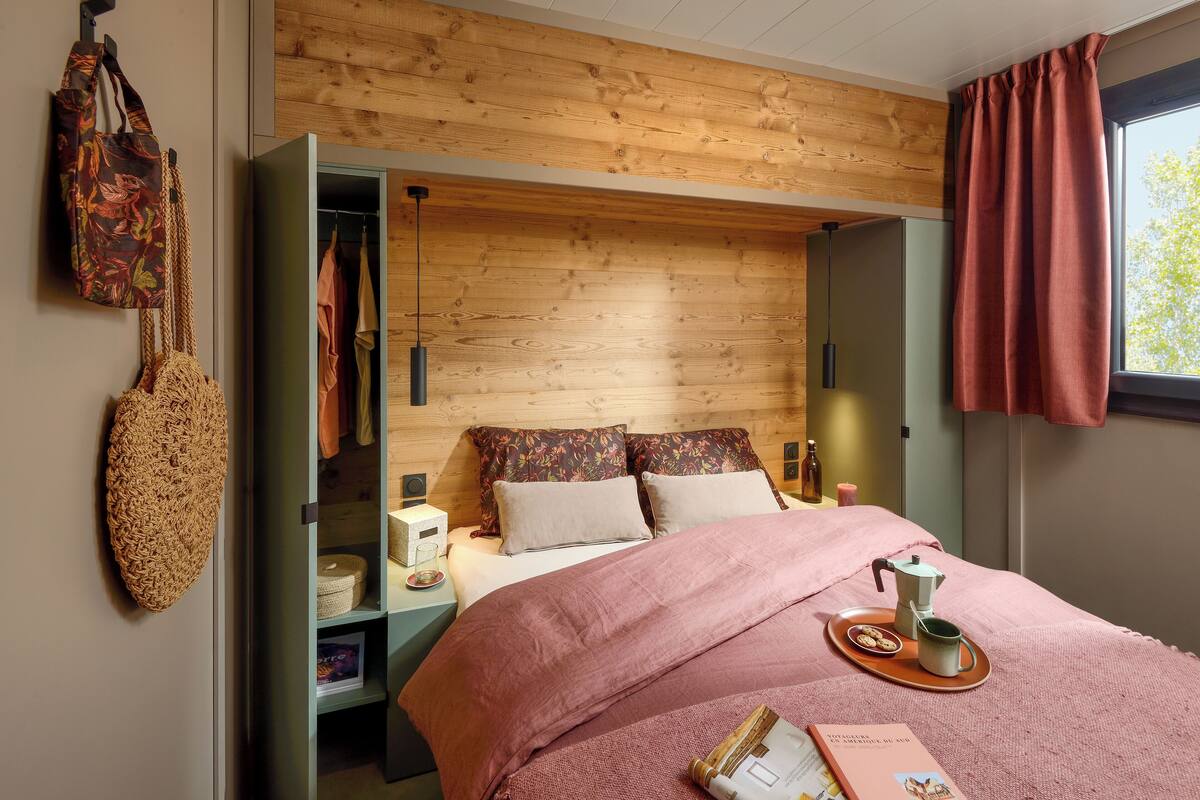 Ein modernes Schlafzimmer mit einem hölzernen Kopfende, einem Bett mit rosa Bettwäsche, einem Nachttisch mit Lampe und einem Fenster mit Vorhängen.