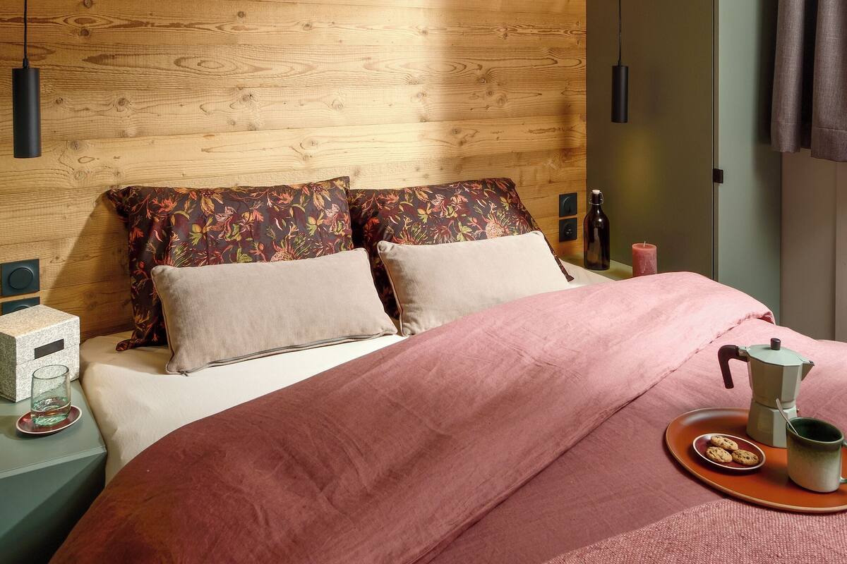 Ein Schlafzimmer mit einem hölzernen Kopfteil, einem Bett mit rosa Bettwäsche, einem Nachttisch mit einem Glas und einem Buch auf dem Boden.