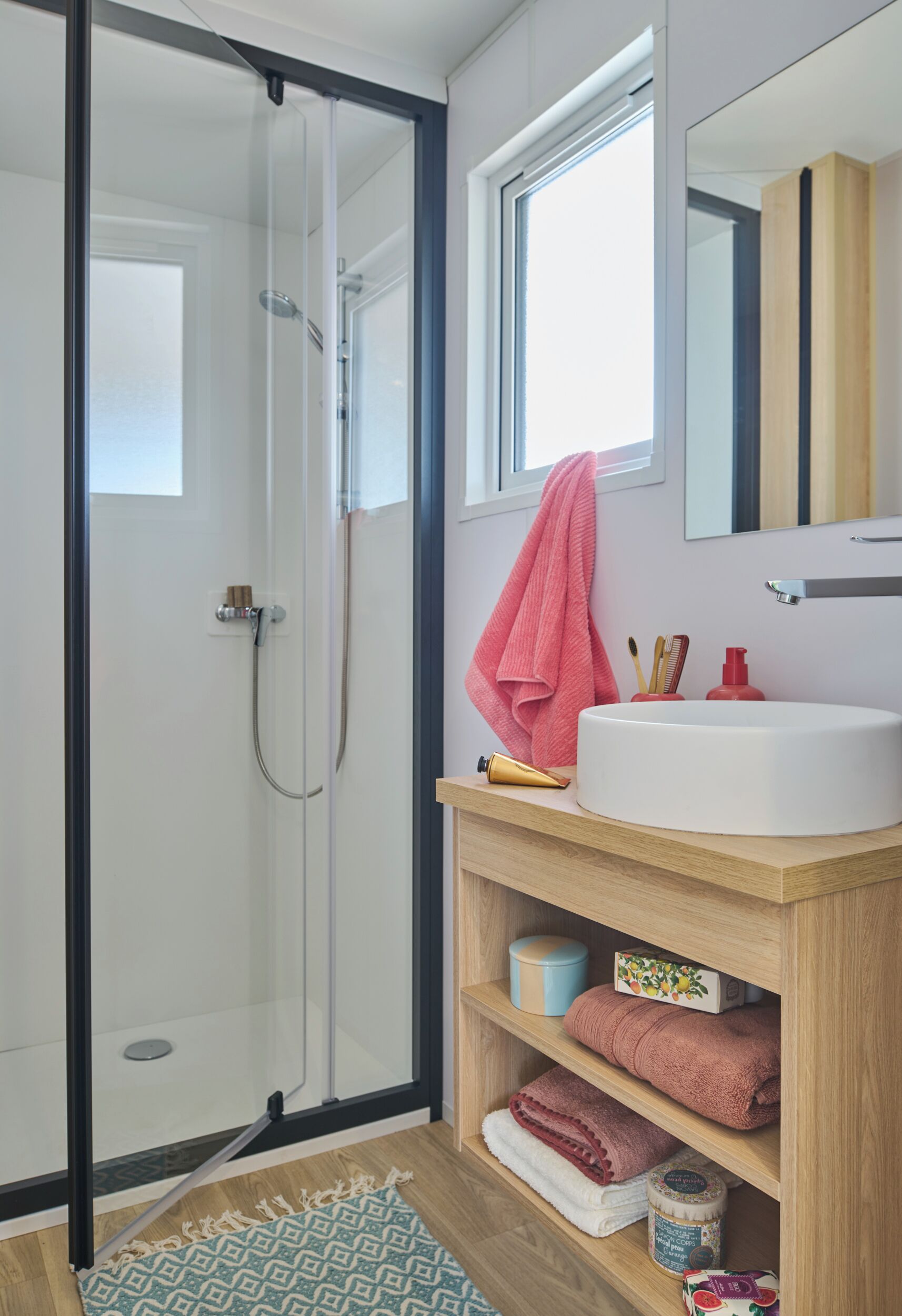 A modern bathroom with a glass shower enclosure, a white sink with a wooden vanity, and a mirror above the sink.