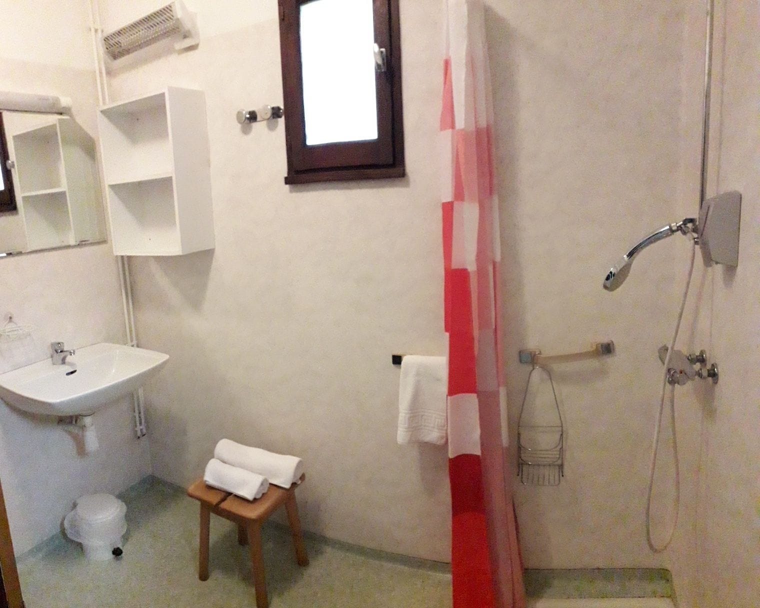 A bathroom with a sink, mirror, towel rack, shower, and a small stool.