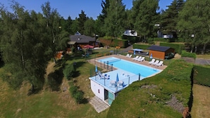 A swimming pool with lounge chairs, surrounded by a fenced area and trees. - VVF Aubrac, Chaudes-Aigues (Chaudes-Aigues)
