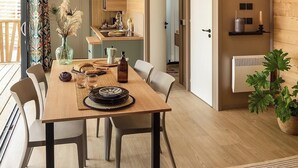 A modern dining area with a wooden table, chairs, and a view of the kitchen. - VVF Aubrac, Chaudes-Aigues (Chaudes-Aigues)