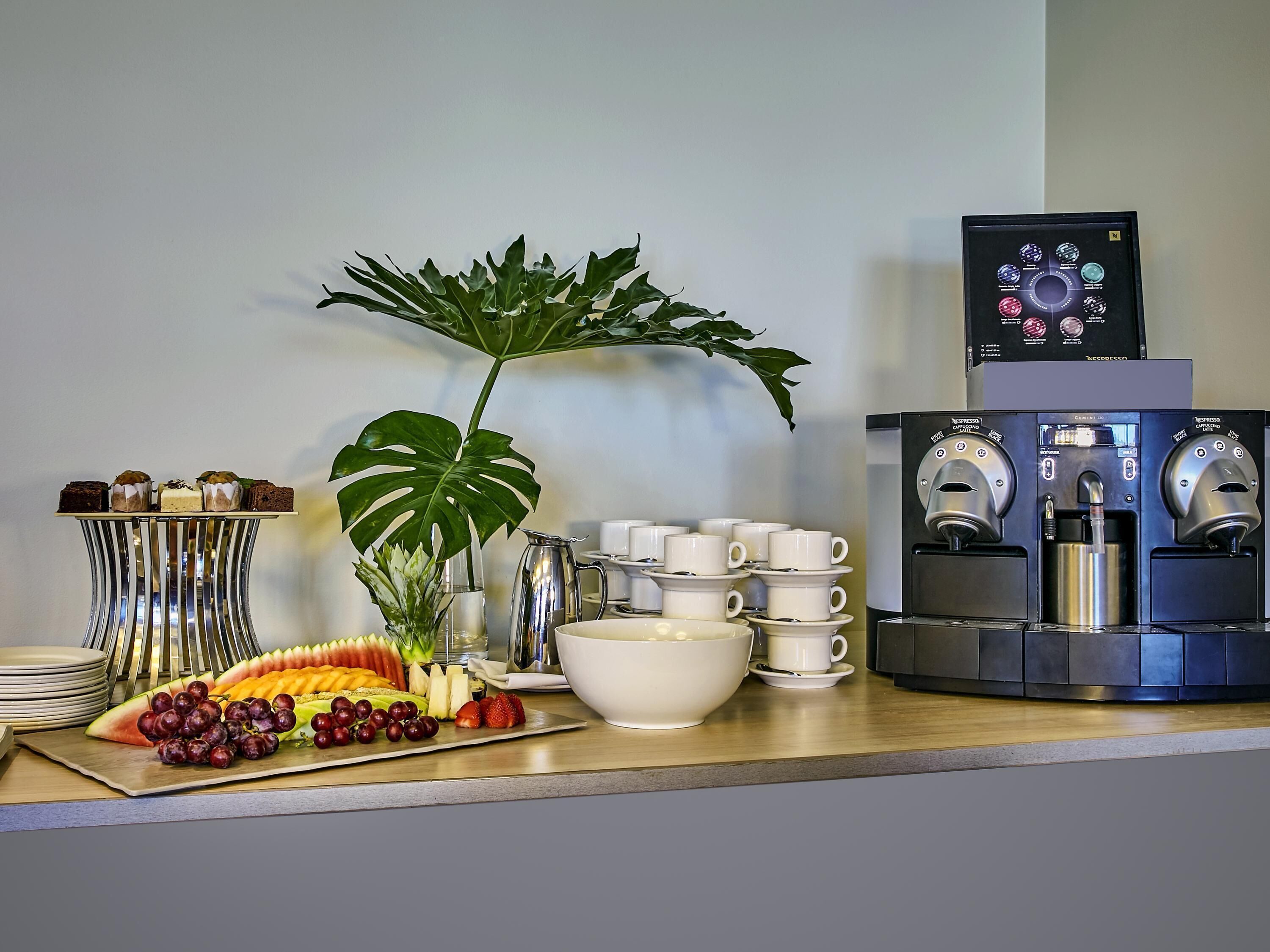 Una estación de café con varios dispensadores, una bandeja de frutas y una planta.