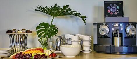 Una estación de café con varios dispensadores, una bandeja de frutas y una planta.