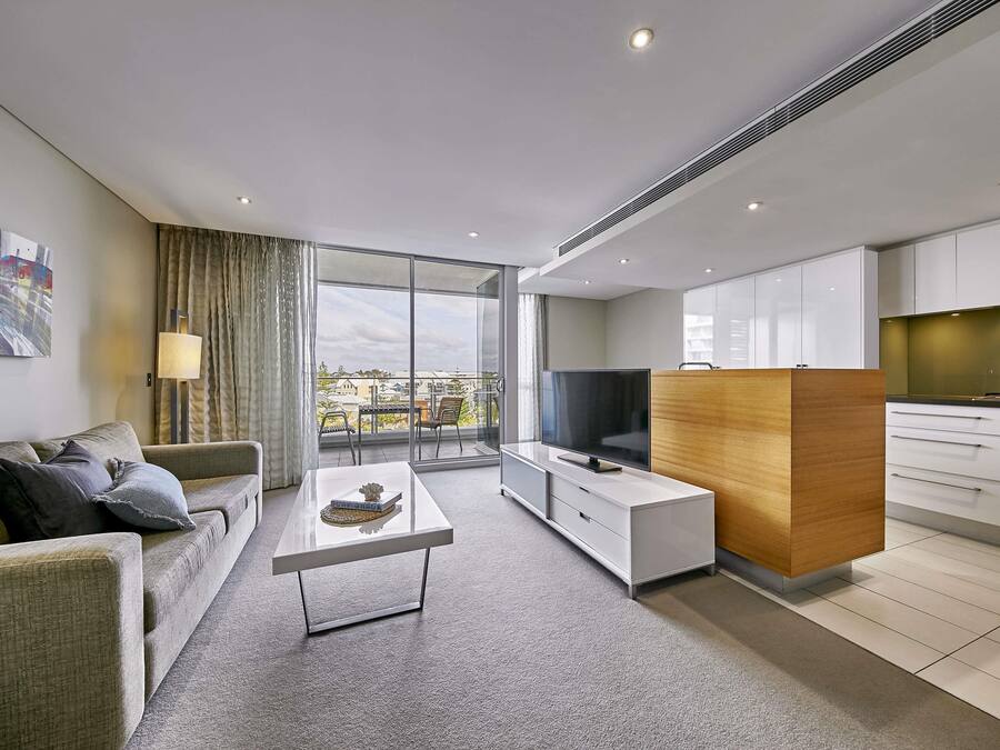 Quarto de hotel moderno com varanda, televisão de tela plana, armário de madeira e sofá.
