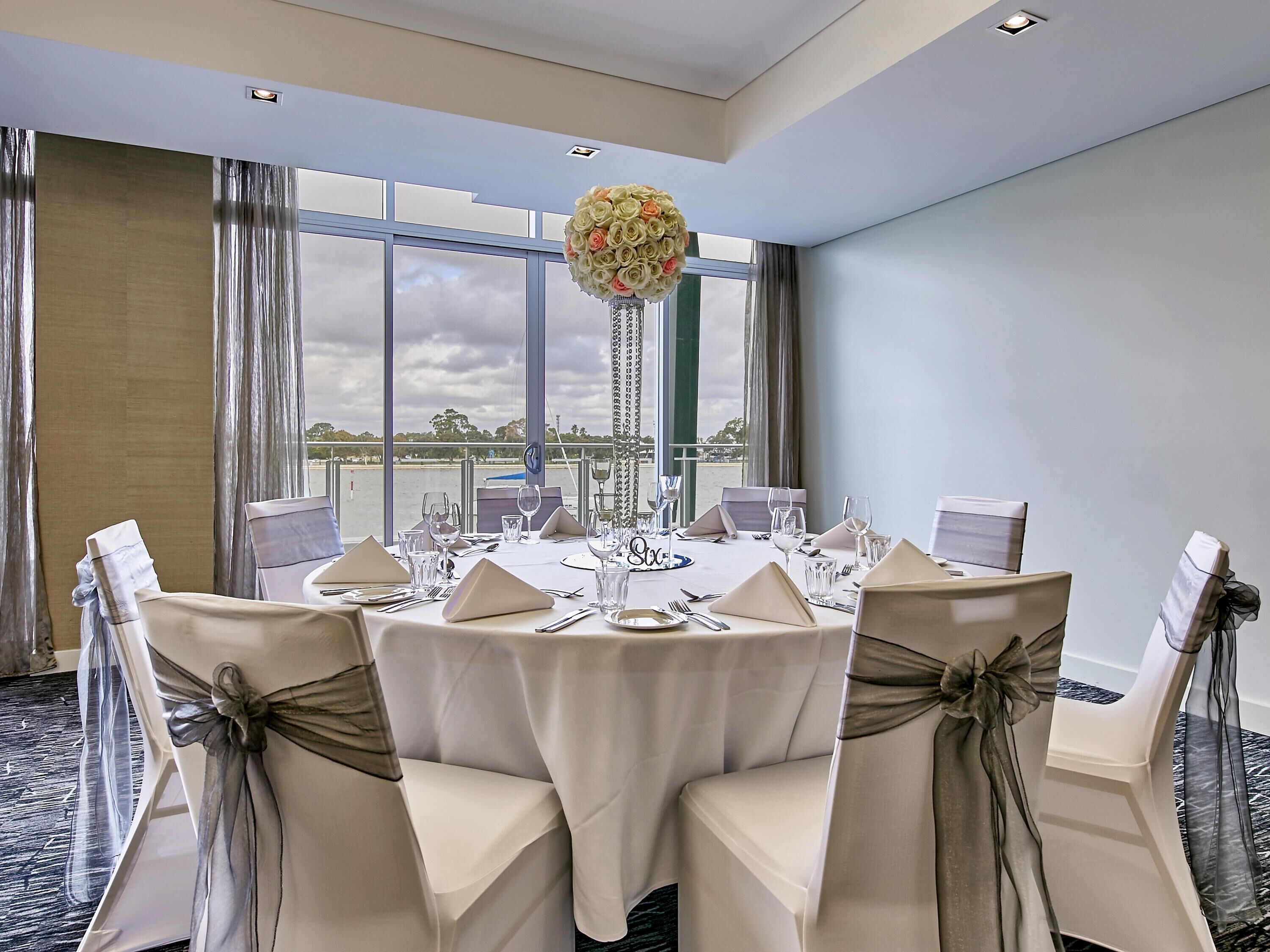 A conference room with a round table set for a meeting, large windows with a view, and a chandelier.