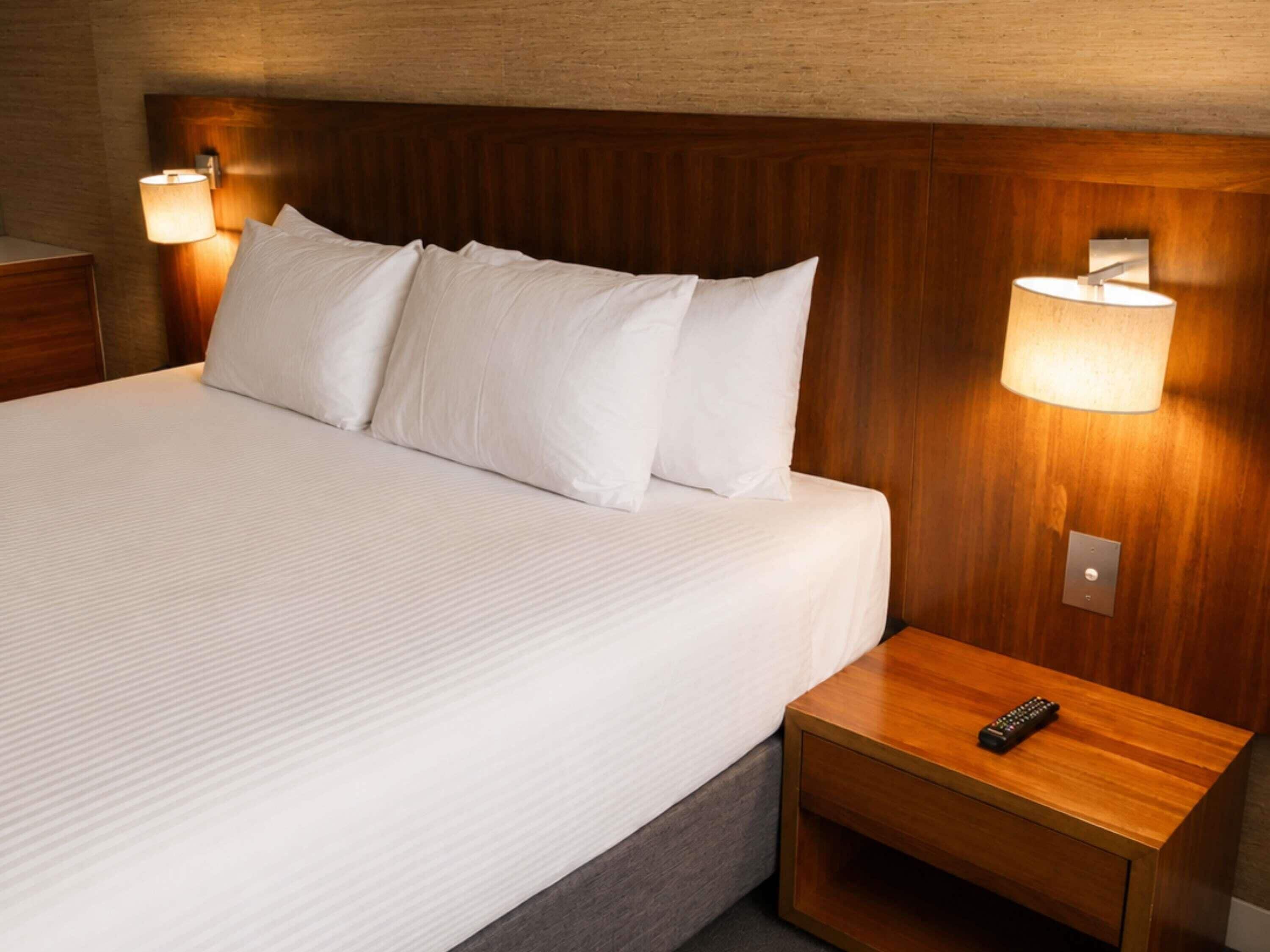 Ein Hotelzimmer mit einem großen Bett, zwei Nachttischlampen, einem Nachttisch mit Fernbedienung und einem Holzkopfstück.