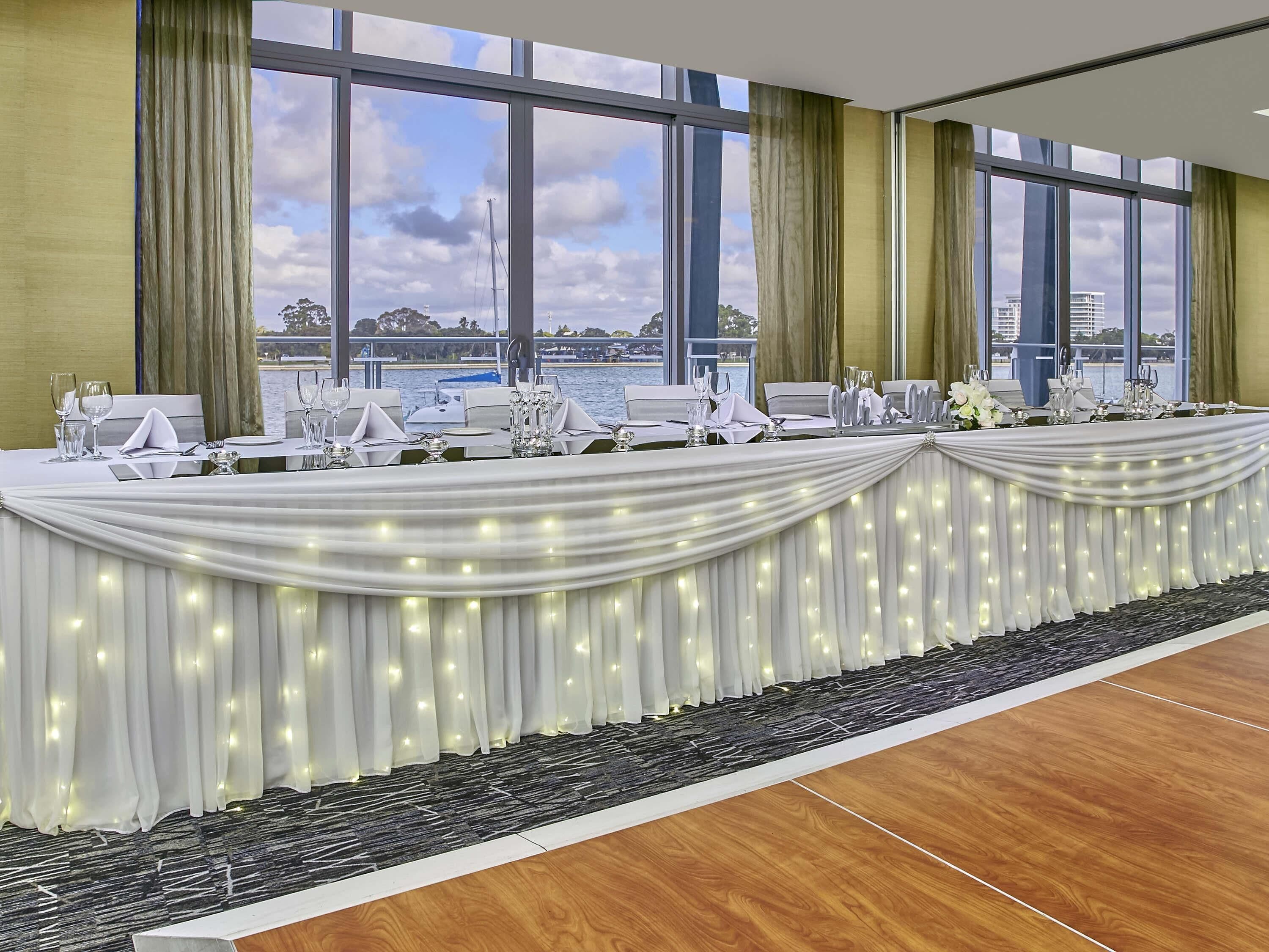 A conference room with a long table set for a meeting, large windows with a view of a body of water and buildings, and a carpeted floor.